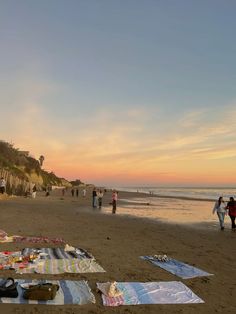 people are walking on the beach at sunset with their surfboards and blankets laid out