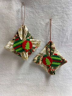 two origami christmas ornaments hanging from strings on a white sheet with red and green decorations