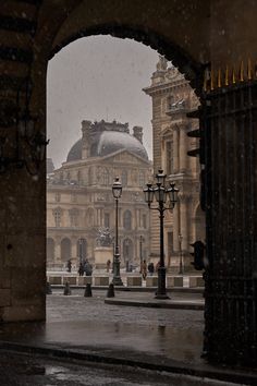 an archway leading to a building with a clock tower in the background and snow falling on the ground