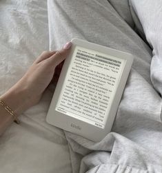 a person's hand holding an electronic device on top of a white sheet covered bed