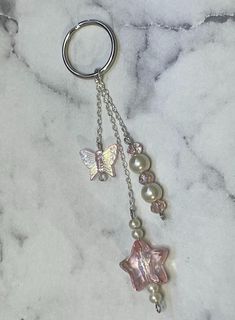 a keychain with two charms attached to it on a marble surface, one has a butterfly and the other has pearls