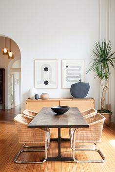 a dining room table with two chairs and a bowl on top of it in front of some art