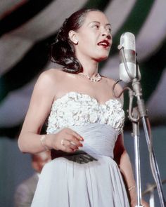 a woman standing in front of a microphone and wearing a white dress with flowers on it