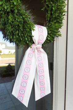 a pink and white bow hanging from the side of a door with green leaves on it