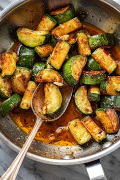 a pan filled with cooked zucchini on top of a marble counter next to a wooden spoon