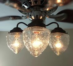 three lights are hanging from the ceiling in front of a ceiling fan with glass shades