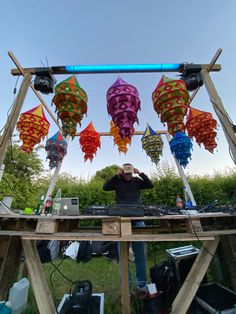 a man standing in front of a wooden structure with many colorful kites hanging from it