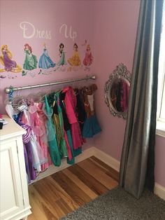 there are many princess dresses hanging on the rack in this girls's room with pink walls