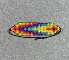 a multicolored beaded surfboard on a gray surface with a black string