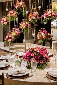 the table is set with place settings and flowers in vases hanging from the ceiling