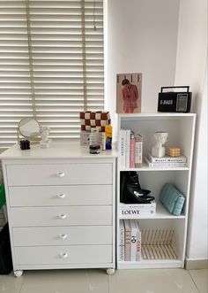 a white book shelf with books, magazines and other items on it next to a window