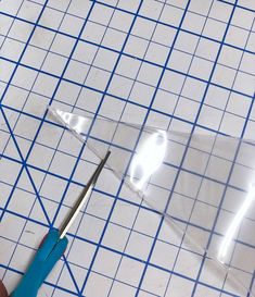 a pair of scissors cutting through clear plastic on a table with blue squares and lines