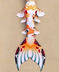 a colorful fish shaped object hanging on the side of a brown wall next to a hand