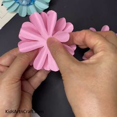 two hands are holding pink and blue paper flowers