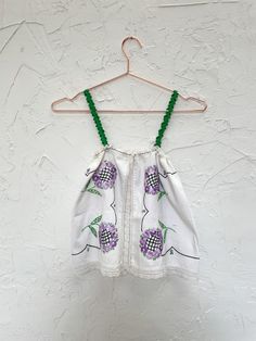 a white top with green beads hanging on a hanger