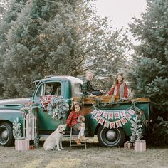 an old green truck with people and a dog sitting in the back, decorated for christmas