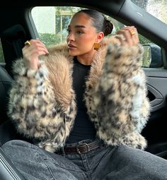 a woman sitting in the passenger seat of a car wearing a leopard print fur coat