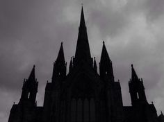 the silhouette of a gothic church against a cloudy sky with full moon in the background