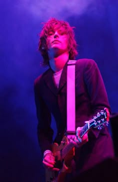 a young man playing an electric guitar in front of purple lighting at a music concert