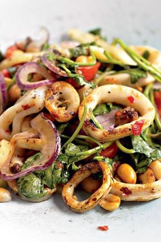 a white plate topped with pasta and veggies covered in seasoning next to red onions