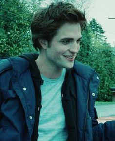 a young man is smiling while sitting on a bench in front of some trees and bushes