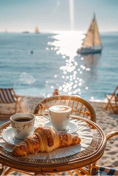 coffee and croissants sit on an outdoor table overlooking the ocean