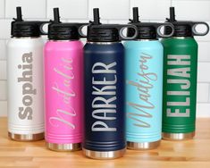 six personalized stainless steel water bottles lined up on a wooden table with white tiles in the background