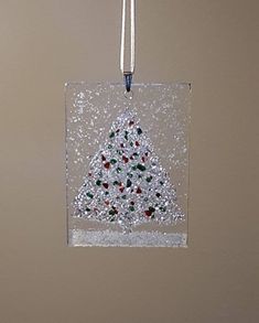 a glass ornament with a christmas tree on it hanging from a cord in front of a wall