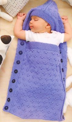 a baby sleeping in a purple blanket on top of a bed next to stuffed animals