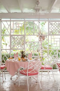 an outdoor dining area with pink chairs and table set for two, surrounded by greenery