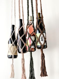 several wine bottles hanging from ropes on a white wall, with one bottle in the middle