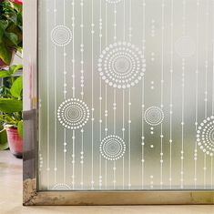 a glass door decorated with white circles and beads on it, next to potted plants