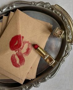 some envelopes with lipstick on them are sitting in a silver tray next to a lighter