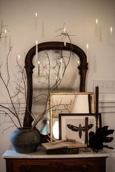 a table topped with a vase filled with branches and candles next to a framed mirror