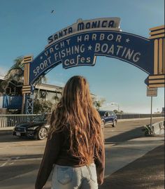 a woman walking under a sign that reads santa monica yacht harbor, sport fishing and boating