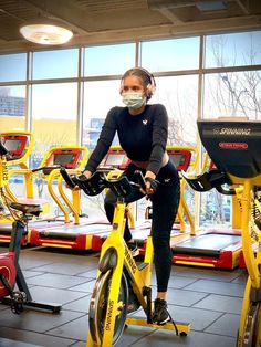 a woman wearing a face mask while riding an exercise bike in a gym with stationary bikes