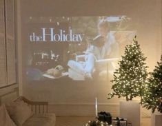 a living room with a christmas tree in front of a large holiday card on the wall