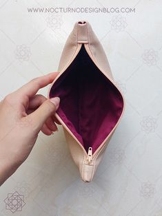 a hand holding an open pink purse on top of a white surface with a purple lining