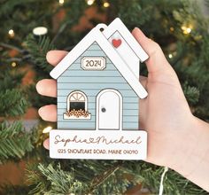 someone holding up a house ornament in front of a christmas tree