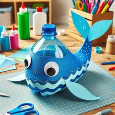 a blue whale shaped water bottle sitting on top of a table next to scissors and markers