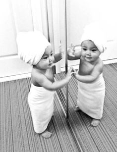 two babies are standing in front of a mirror with towels on their heads and arms