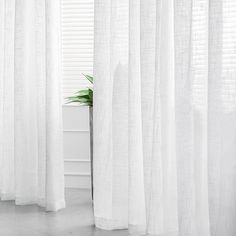 a white curtain in front of a window with a potted plant next to it