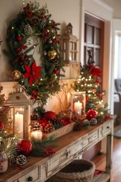 christmas decorations on a table with candles and wreaths in front of the fireplace mantle