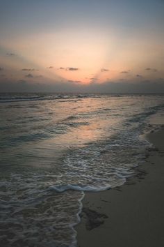 the sun is setting over the ocean with waves coming in from the shore and sand on the beach