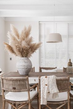 a dining room table with chairs and a vase filled with pamodia in it