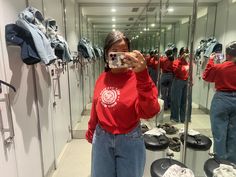 a woman taking a selfie in front of a mirror with clothes hanging on the wall