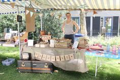 a woman standing next to a table with boxes on it in the grass under a tent