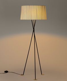 a floor lamp with a white shade on it and a black cord plugged into the base