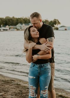 a man and woman hugging on the beach with water in the backgrouds