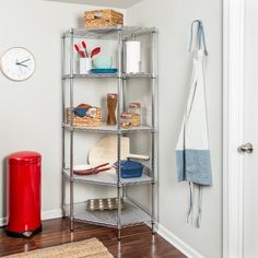 a metal shelf filled with lots of items next to a red trash can and clock